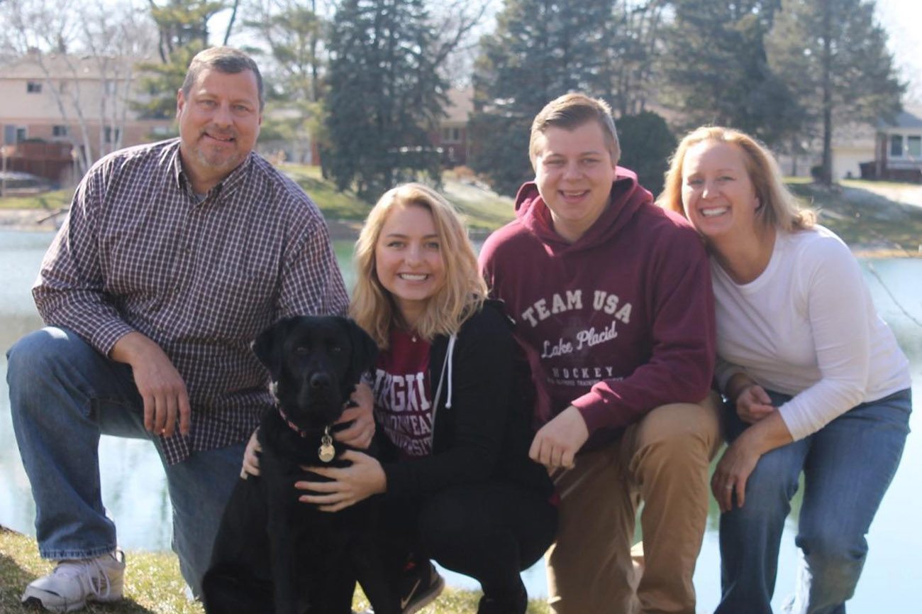 The Williams family kneels outdoors with a black lab